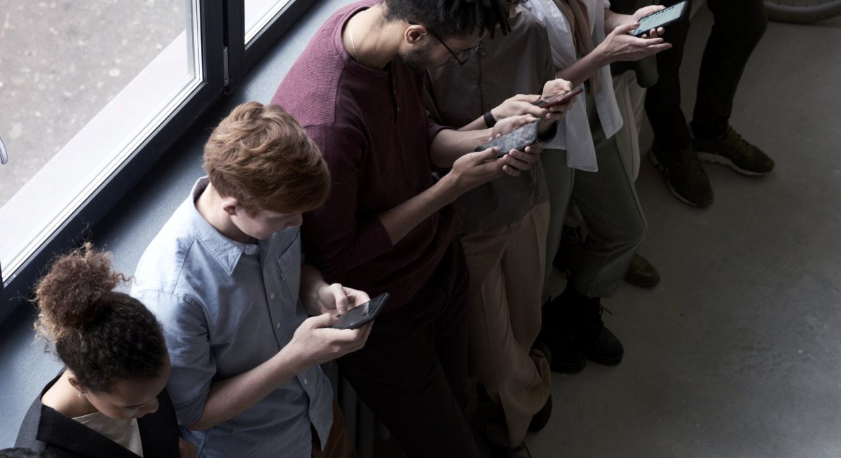 Grupo de pessoas lado a lado, cada uma olhando o próprio celular, vistas de cima